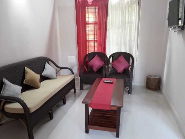 A living room with a sofa, two armchairs, a coffee table, and a TV mounted on the wall.