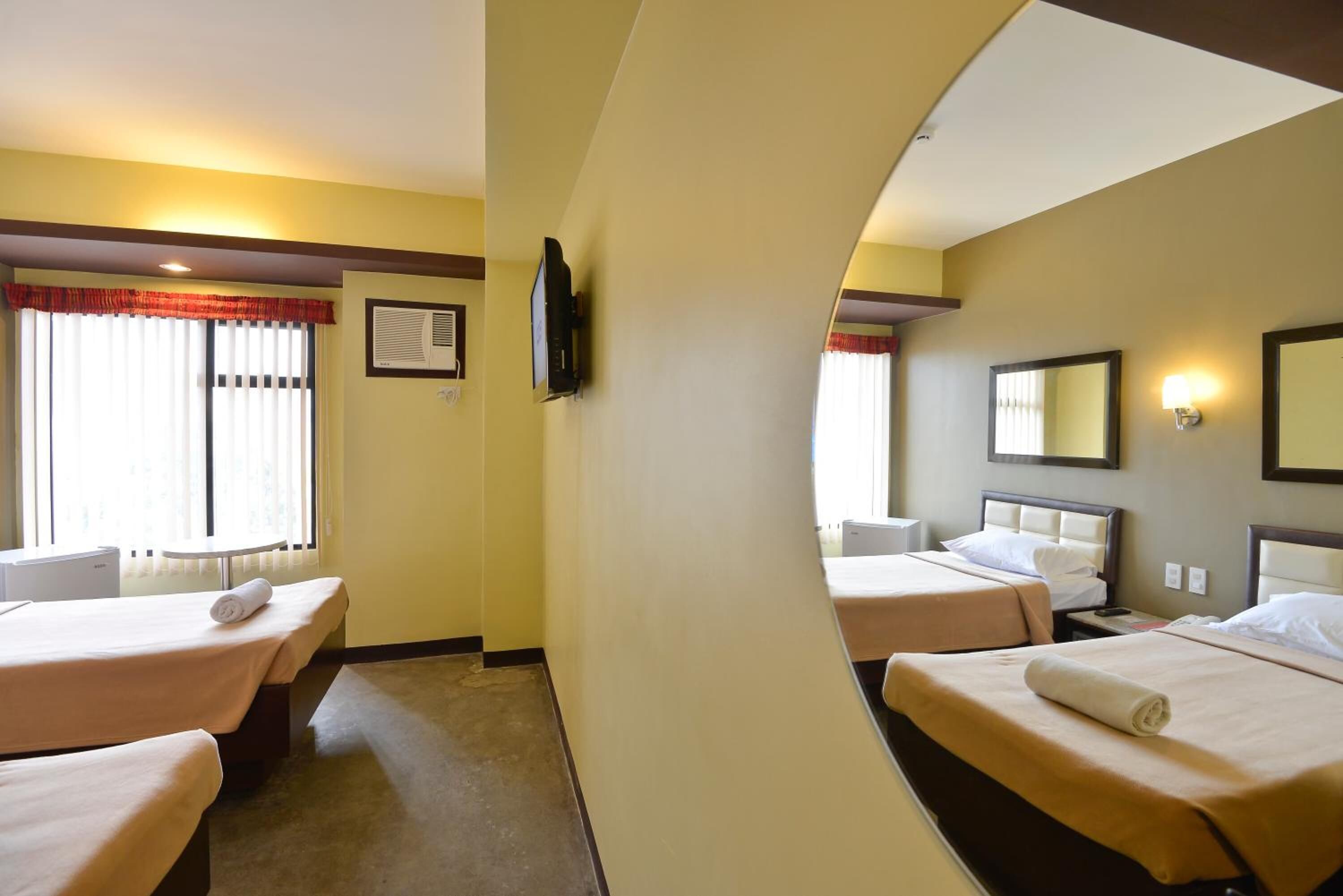 Una habitación de hotel con dos camas, televisión, espejo y ventana con cortinas.