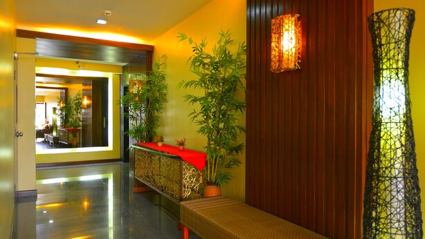 A hotel lobby with a reception desk, a bench, a large potted plant, and a decorative wall lamp. - Express Inn - Cebu Hotel (Cebu City)