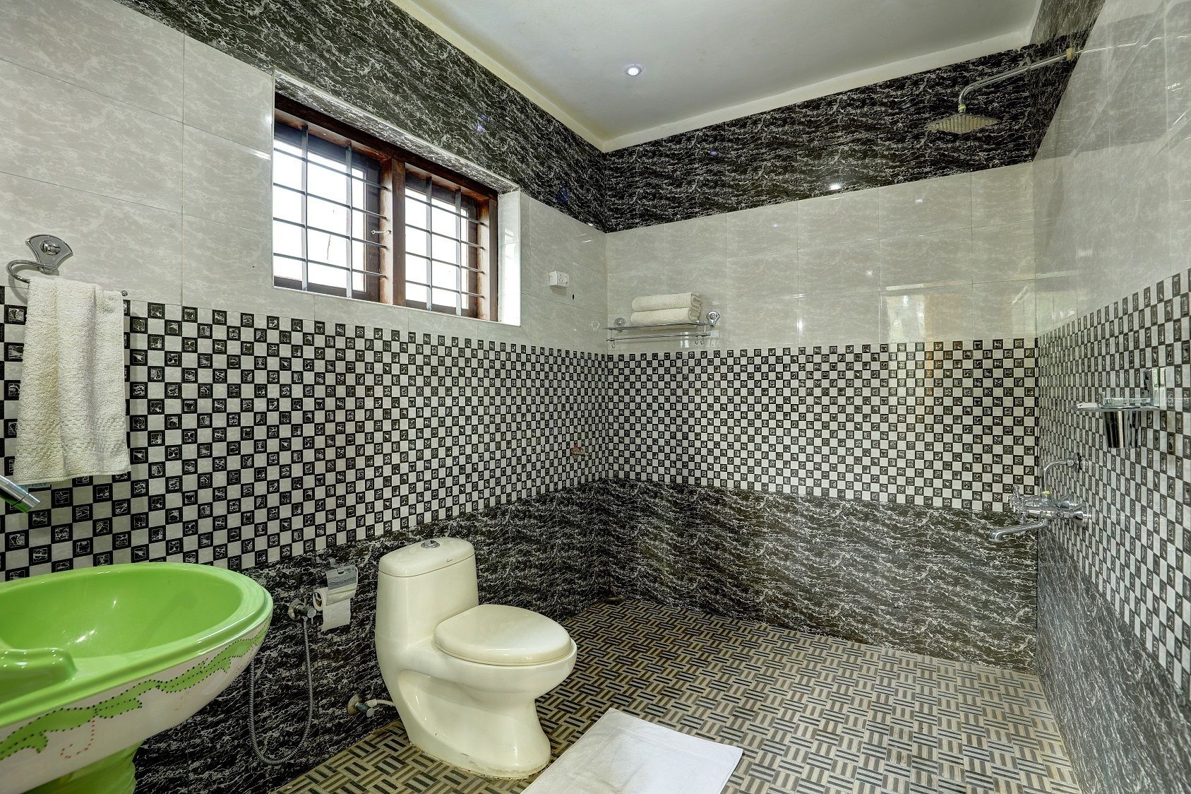 A bathroom with a checkered tile wall, a green sink, a white toilet, and a shower area.