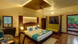 A hotel room with a large bed, a desk with a chair, a window with curtains, and a ceiling fan. - Periyar Nest Resorts (Peermade)