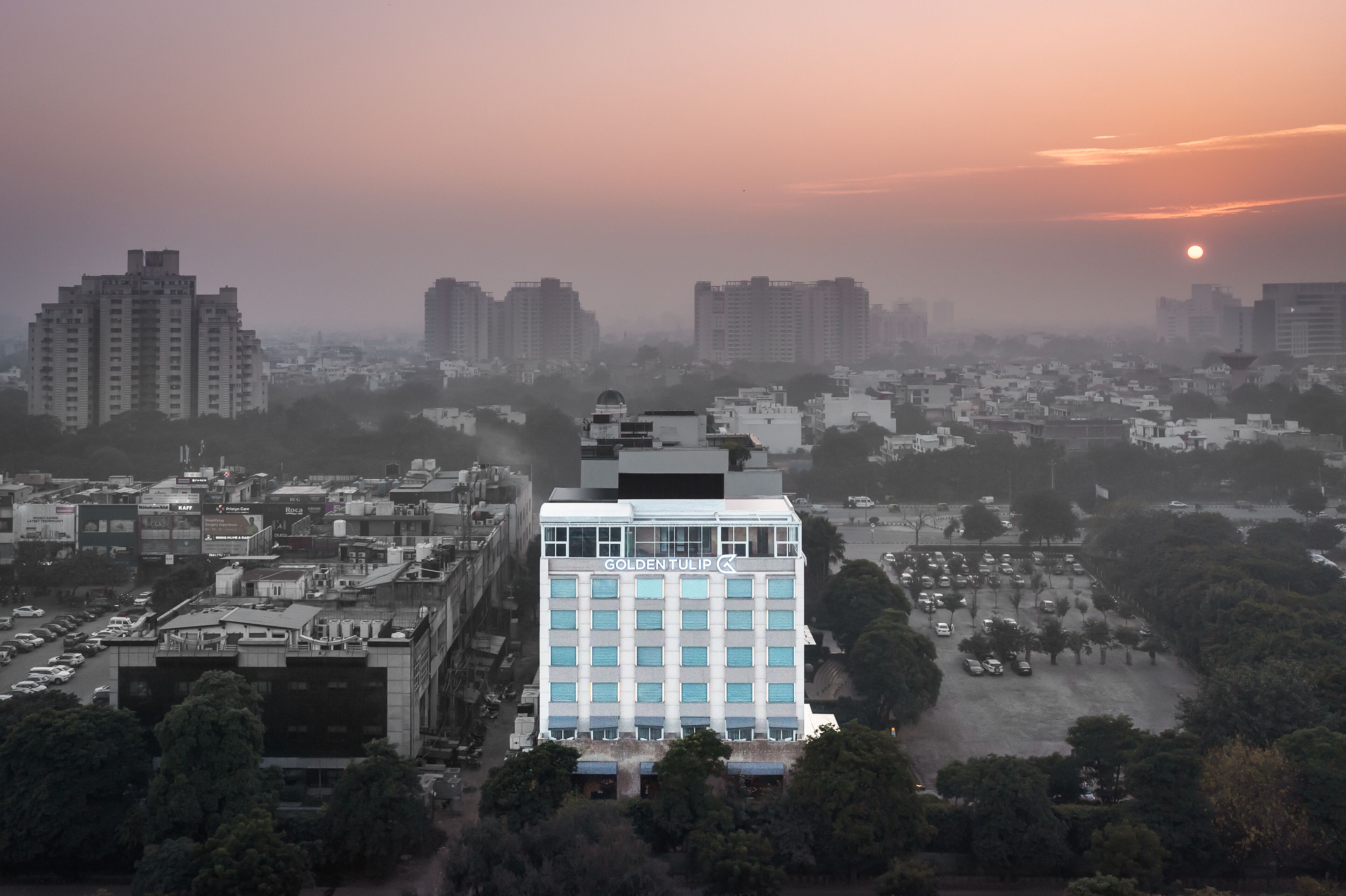 Un grand hôtel, reconnaissable à son imposante enseigne « Golden Tulip », situé dans un quartier urbain dense, entouré d’autres immeubles et de voitures garées.