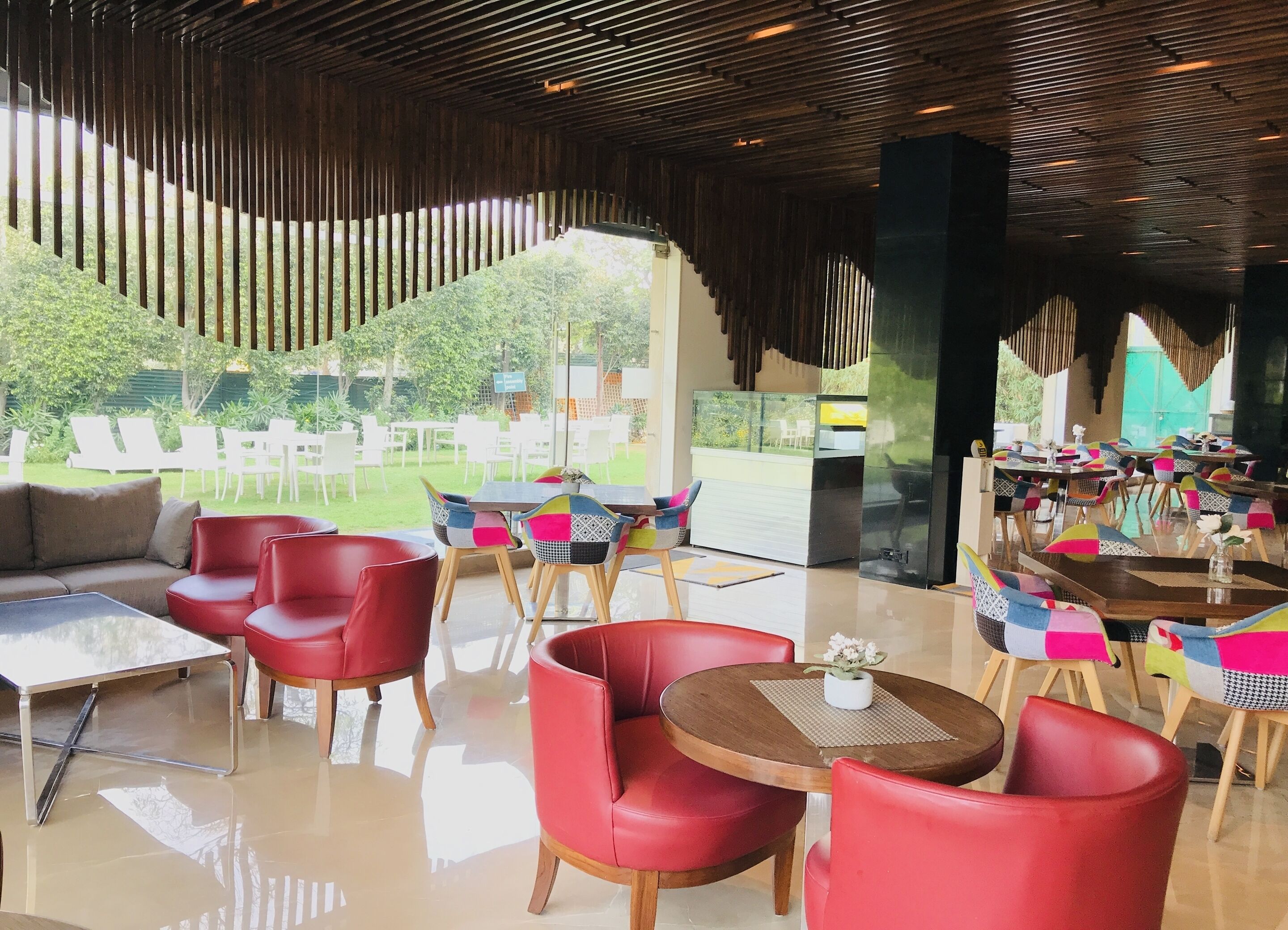 Un espace de restauration intérieur moderne, avec des chaises et des tables rouges, de grandes fenêtres donnant sur l’extérieur et un plafond en bois.