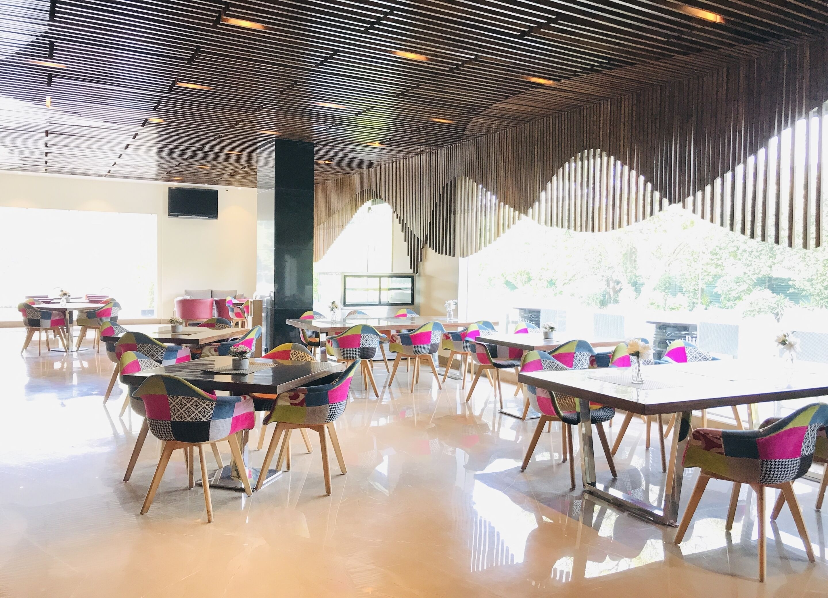 A spacious indoor area with tables and chairs, a high ceiling with a patterned design, and large windows allowing natural light.