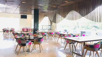 A spacious indoor area with tables and chairs, a high ceiling with a patterned design, and large windows allowing natural light.