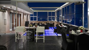 A modern restaurant with a high ceiling, large windows, and a city view at night. - Golden Tulip Gurgaon - Sector 29 (Gurugram)