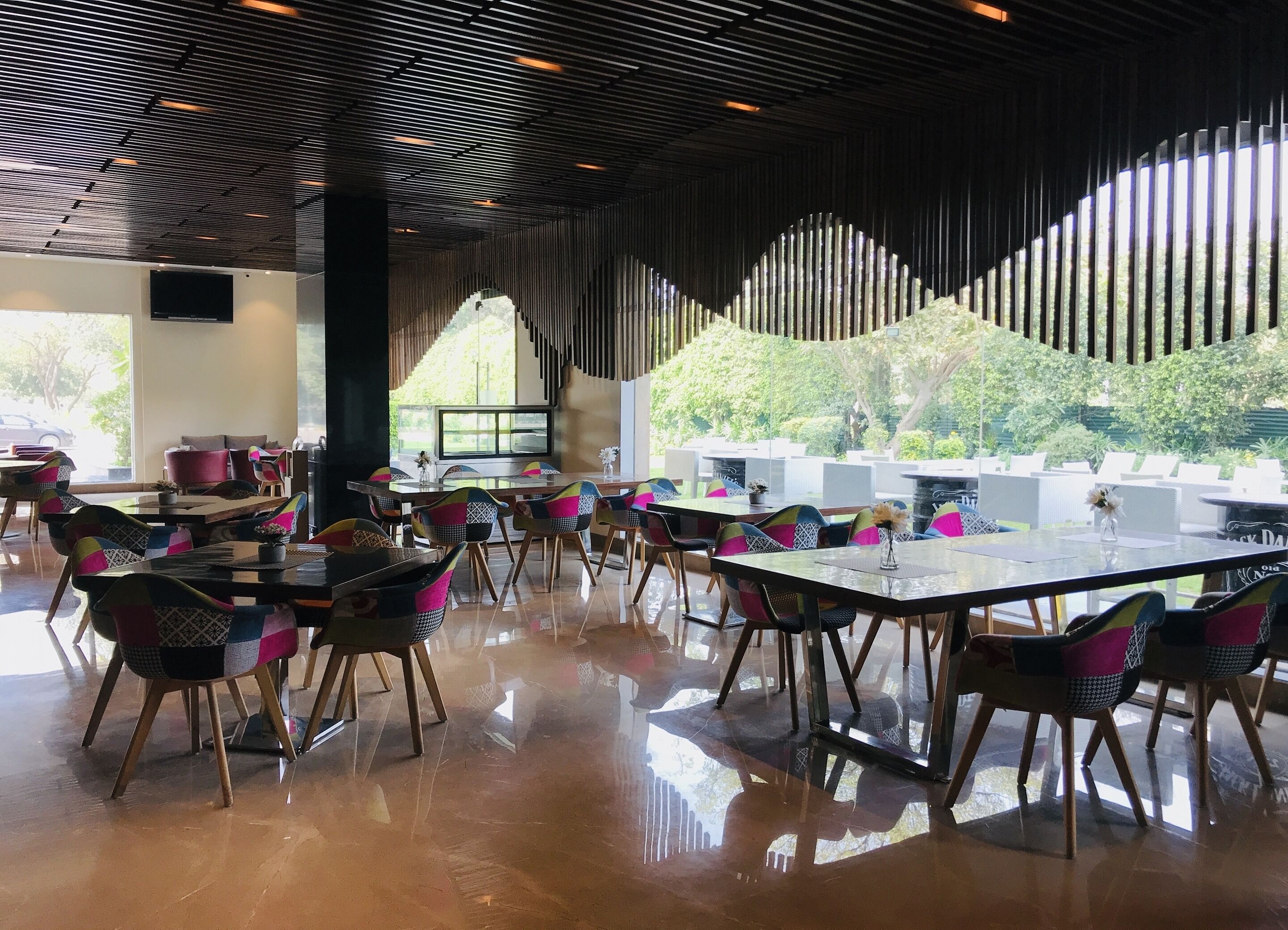 Un espacio interior amplio con mesas y sillas, ventanas grandes con vistas a zonas verdes y un diseño de techo moderno.