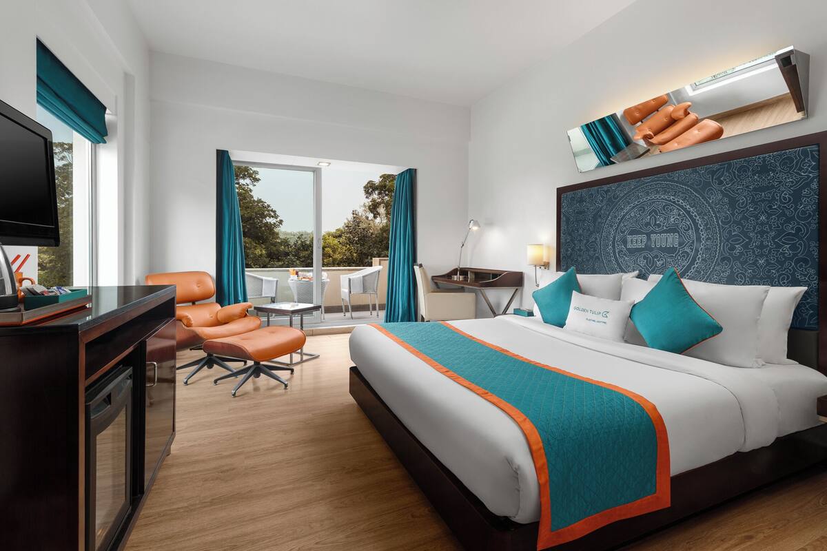 Habitación de hotel con una cama grande, un escritorio con televisor, una silla y vistas al exterior.