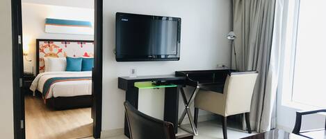 A hotel room with a bed, a desk, a chair, a TV, and a window with curtains.