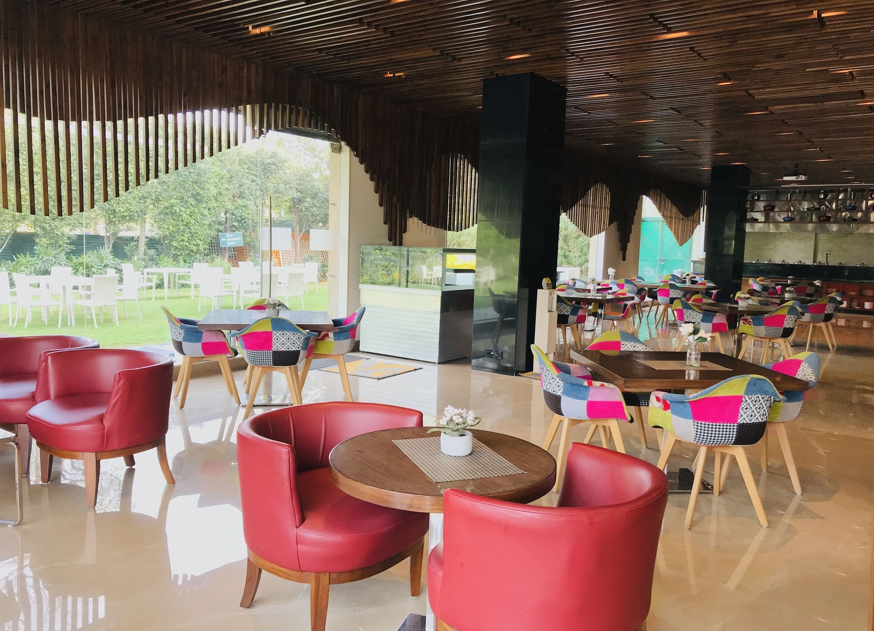 A spacious indoor dining area with red leather chairs and tables, large windows offering a view of the outdoors, and a modern ceiling design.