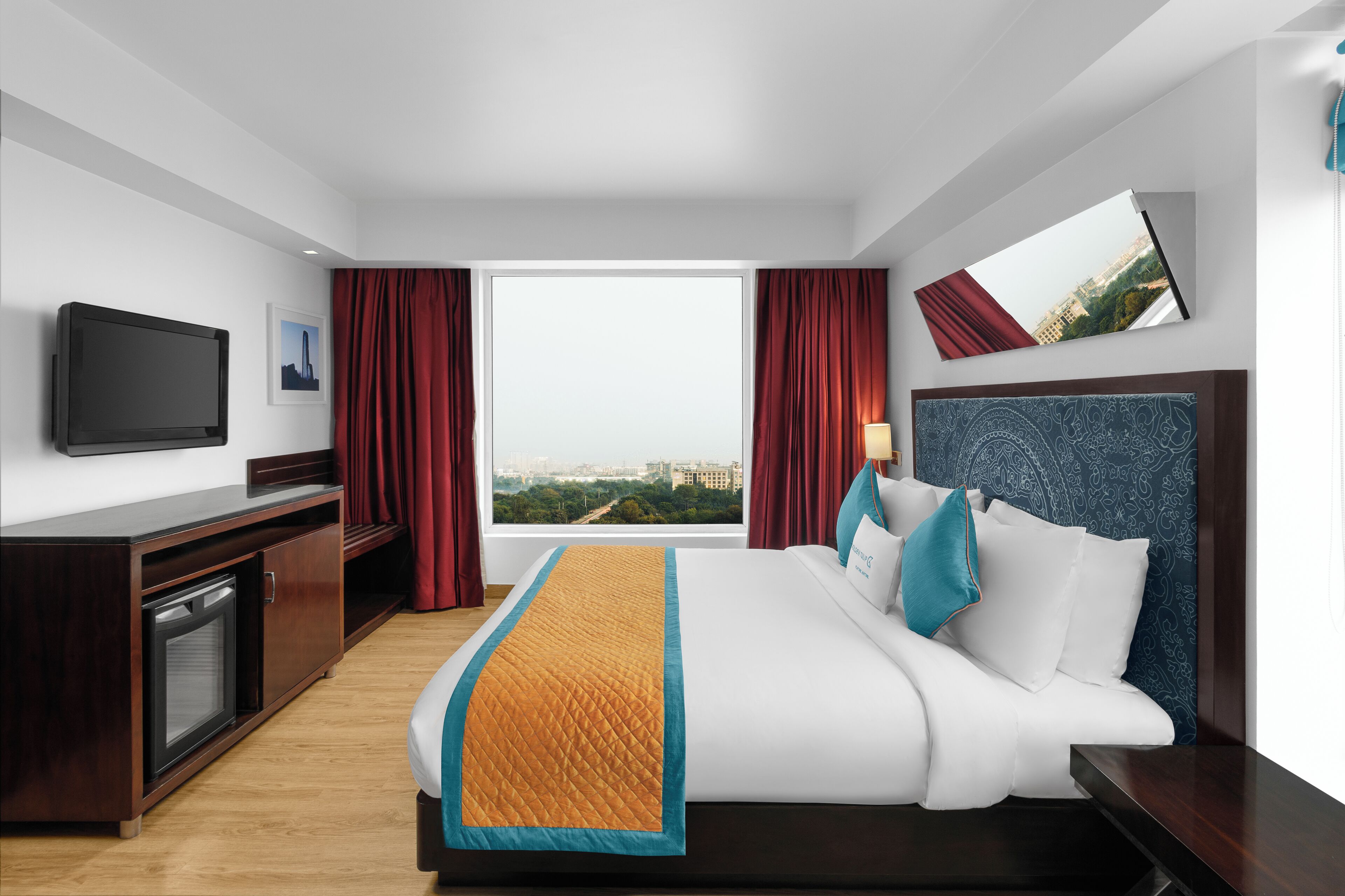 A hotel room with a bed, a TV, a desk, and a window with a city view.
