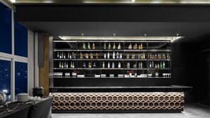 A bar area with shelves of liquor bottles and glasses, a patterned bench, and a table with plates and cutlery. - Golden Tulip Gurgaon - Sector 29 (Gurugram)