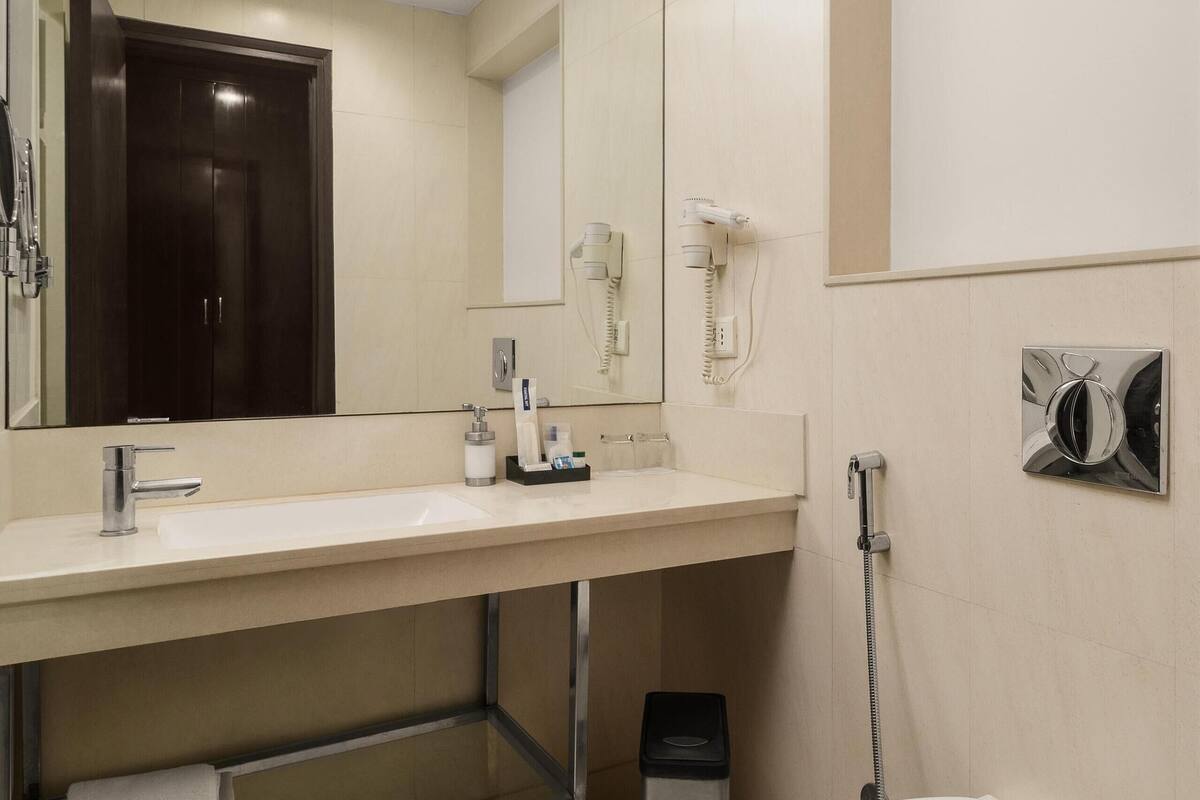 Un baño moderno con lavamanos, espejo, inodoro y un cubo de basura.