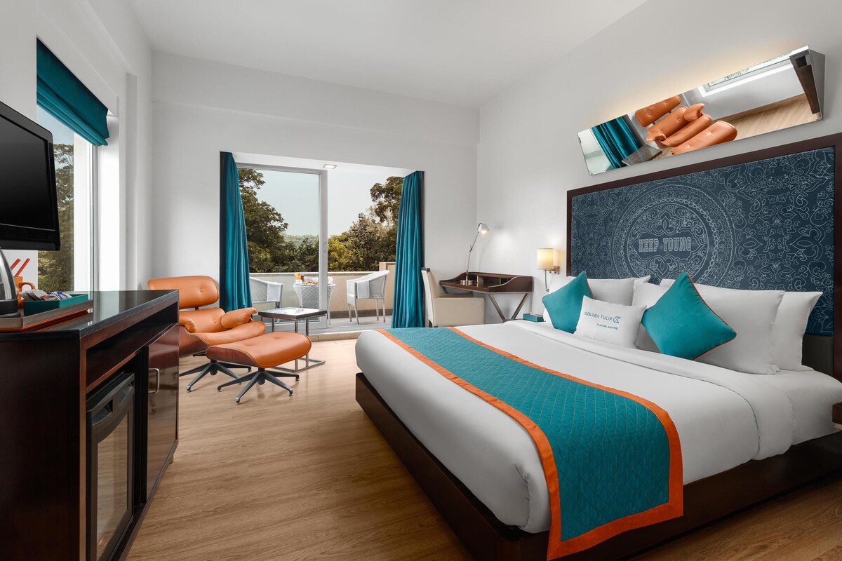 Habitación de hotel con una cama grande, un escritorio con silla, televisión y vistas al exterior.