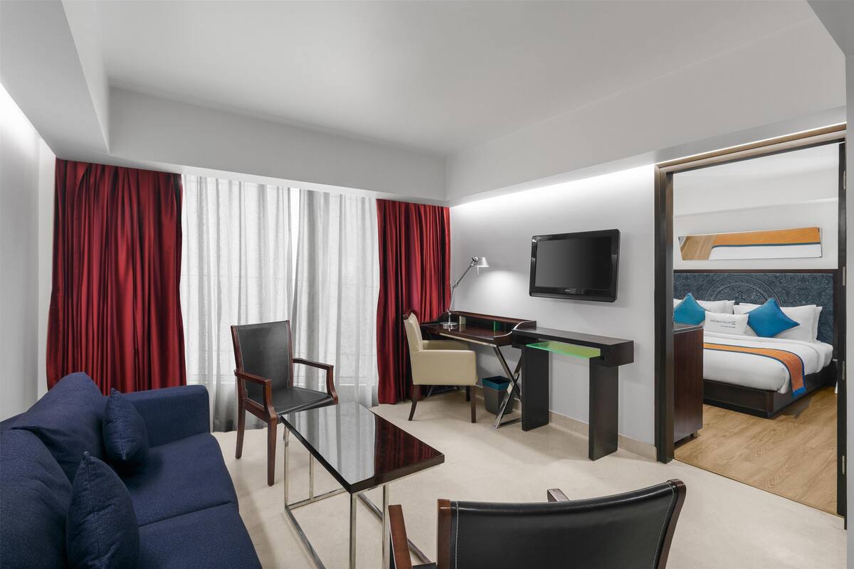Habitación de hotel con sofá, escritorio, silla, televisión y cama con almohadas.