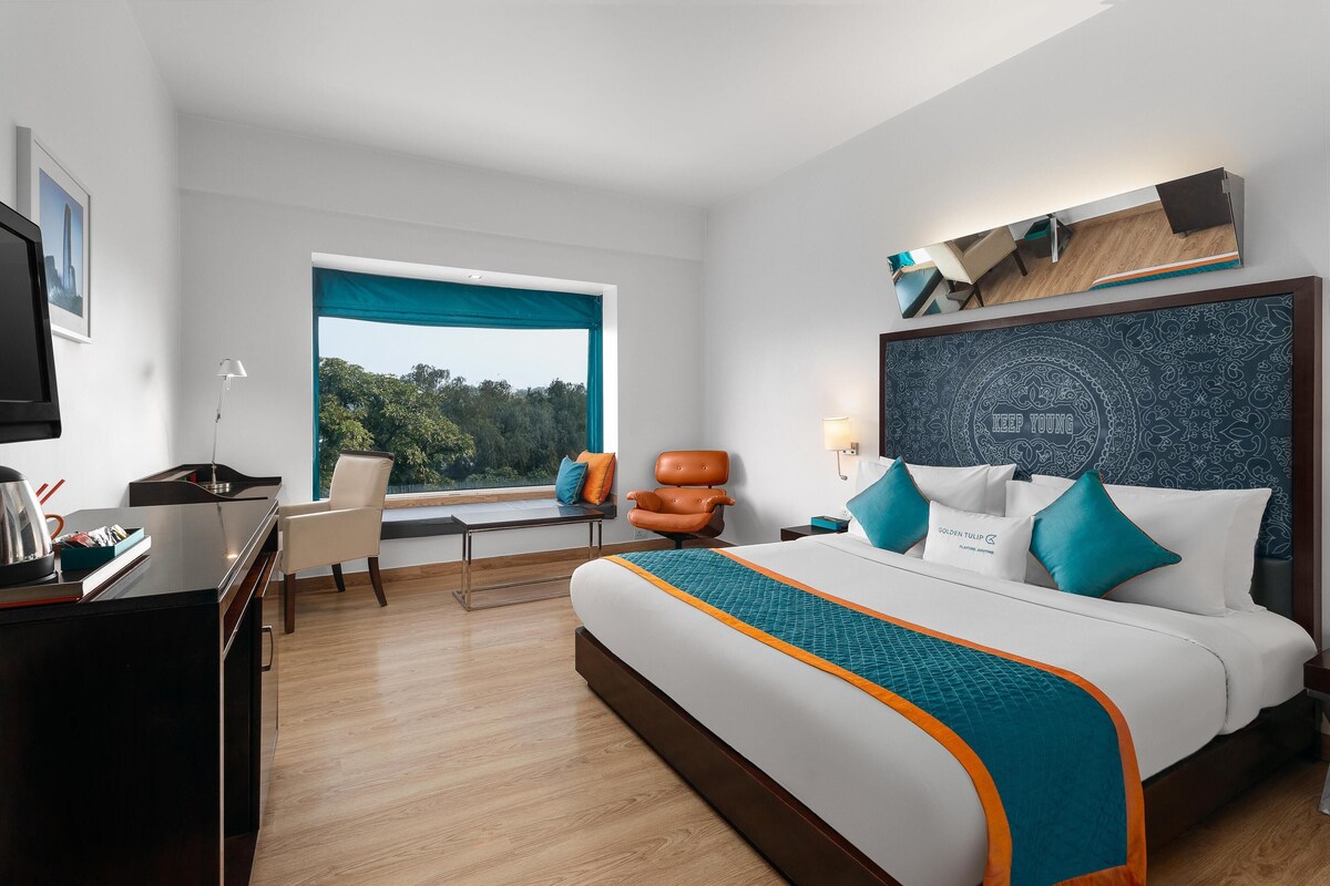 Una habitación de hotel moderna con una cama grande, un escritorio, una silla y una ventana con vistas al exterior.