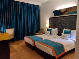 Habitación de hotel con dos camas, un escritorio, una silla y un ventanal con cortinas.