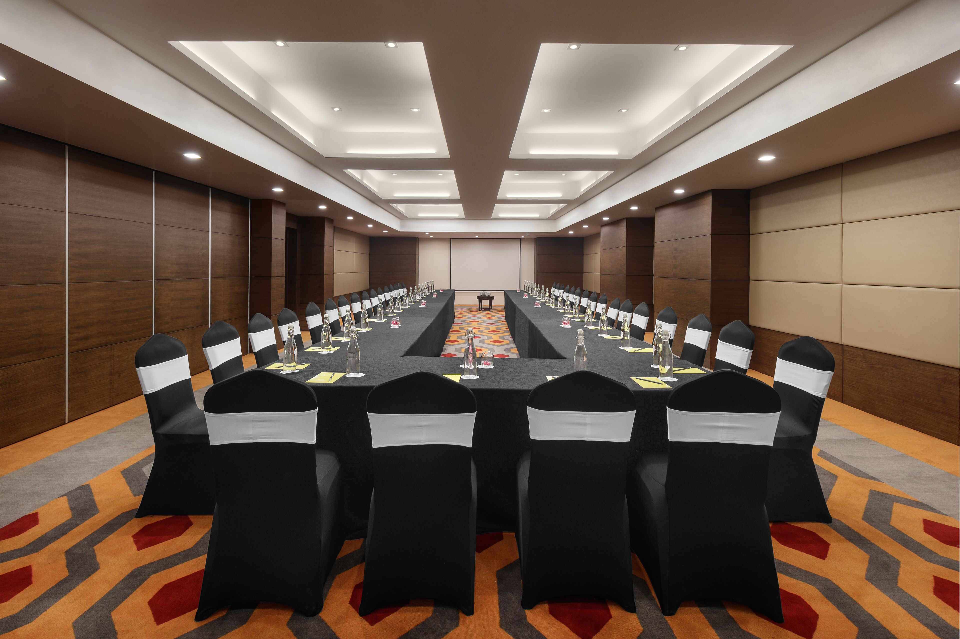 A conference room with a long table, black chairs with white sashes, and a carpeted floor.