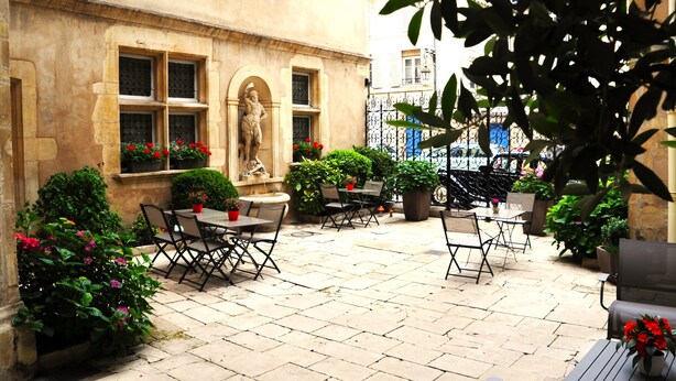 Un café en plein air avec un sol en pierre, des tables, des chaises et des plantes en pot.