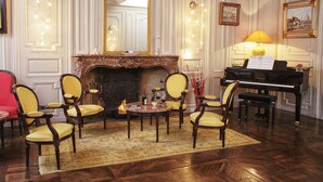 Une pièce élégante, dotée d’un grand piano, de fauteuils richement décorés, d’une cheminée et d’un grand miroir.