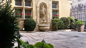 Une cour agrémentée d’une statue, de plantes en pot et d’un portail en fer forgé.