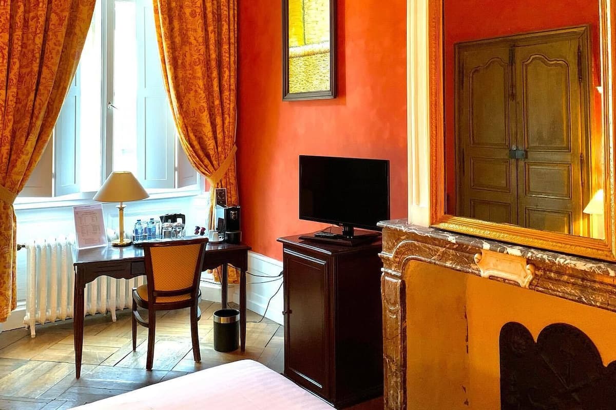 A hotel room with a desk, chair, TV, and a bed.