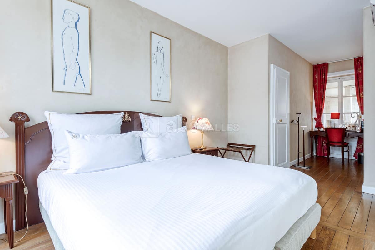 A neatly made bed with white linens, a wooden headboard, and two wall-mounted artworks.