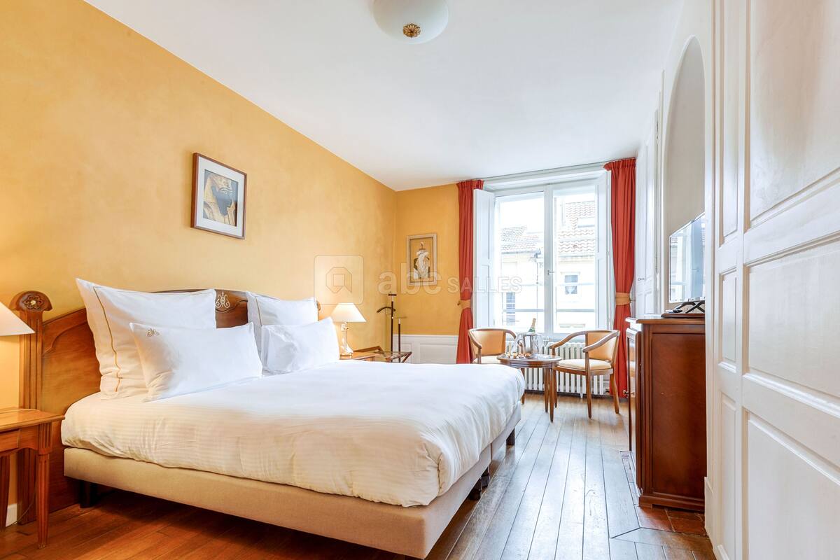 A hotel room with a large bed, a desk, a chair, and a window with curtains.