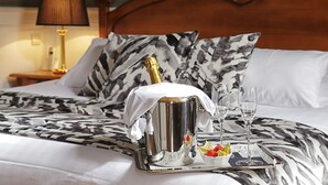Un lit avec un seau à champagne, deux verres et un plateau de fruits posé sur une couvre-lit à motifs.