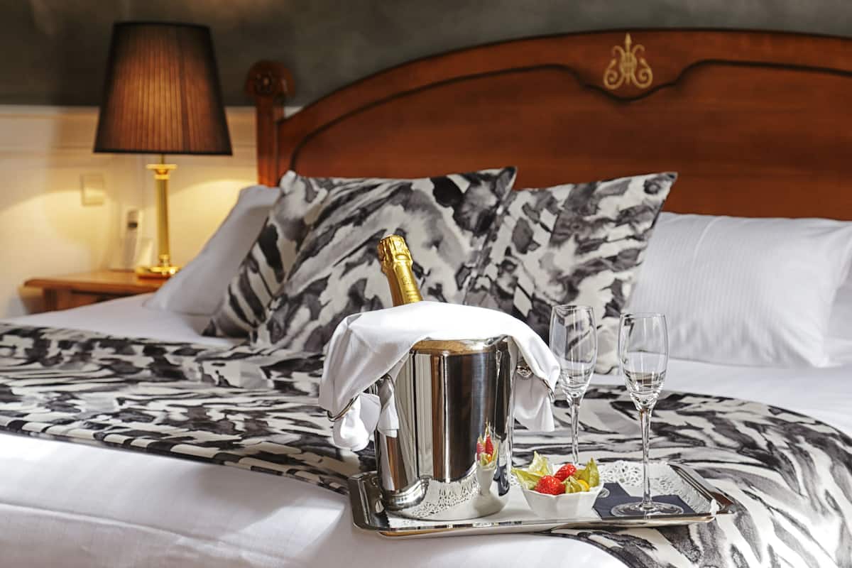 A bed with a champagne bucket, two glasses, and a tray with fruit on a patterned bedspread.
