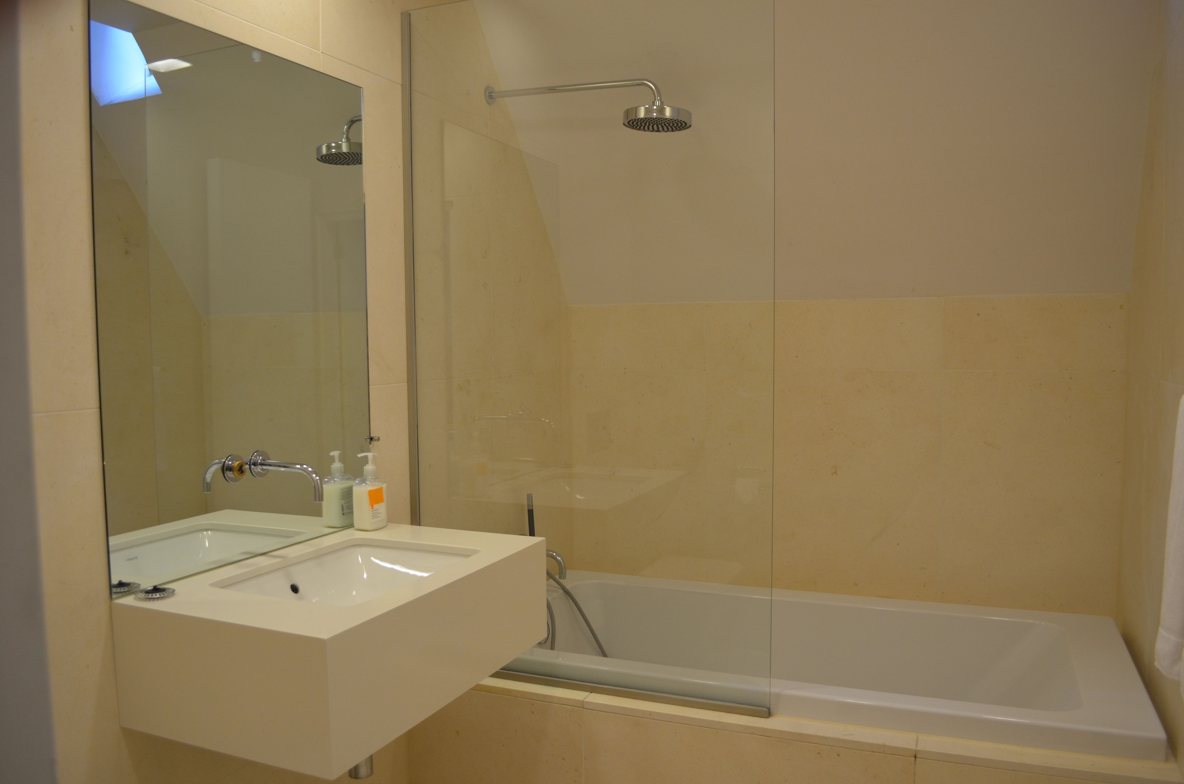 Een badkamer met een wit wastafel, een spiegel, een douchekop en een bad.