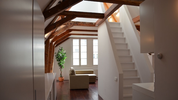 A spacious loft with a high ceiling, exposed wooden beams, a staircase, and a large window providing natural light. - Rembrandtplein B&B (Amsterdam)