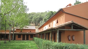 A courtyard with a grassy lawn, a wooden fence, and buildings with a traditional architectural style. - Posada El Camino (Almonaster la Real)