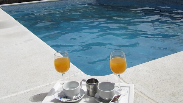 A poolside setting with a tray of two glasses of orange juice, two cups, and a metal pitcher. - Posada El Camino (Almonaster la Real)