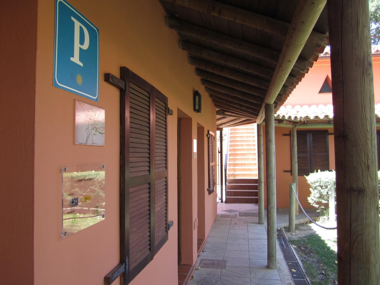 Un pasillo con un letrero azul de estacionamiento, contraventanas de madera y suelo de baldosas.