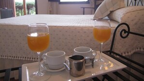A neatly made breakfast tray with two glasses of orange juice, a white mug, and a metal cup on a table in a room with a bed and a window. - Posada El Camino (Almonaster la Real)