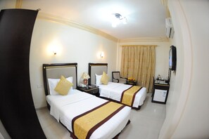 A hotel room with two beds, a small desk, a television, and a minibar. - Cedar Hotel (Aqaba)