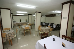 A dining area with multiple tables and chairs, some covered with checkered tablecloths, and a 'No Smoking' sign on the wall. - Cedar Hotel (Aqaba)