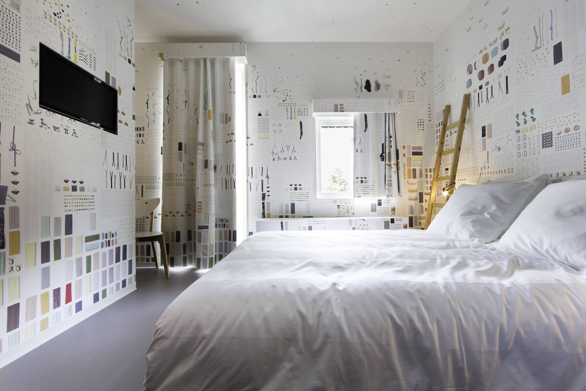 Un dormitorio con una cama grande, un televisor montado en la pared y un baño visible a través de una puerta abierta.