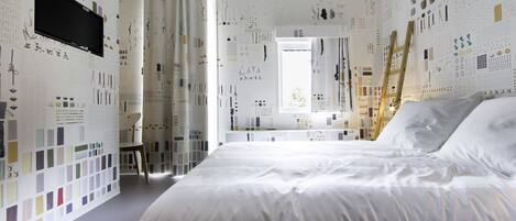 Une chambre avec un grand lit, un téléviseur fixé au mur et une salle de bain visible à travers une porte ouverte.