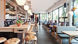 Un área de bar moderna con taburetes de madera, una barra con varias botellas y un espacio de estar con mesas y sillas.