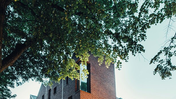 Un edificio moderno con fachada de ladrillo, grandes ventanales y un restaurante visible con mesas al aire libre.