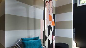 Une chambre moderne avec un mur à rayures, une chaise en métal avec un coussin turquoise et un pouf noir.