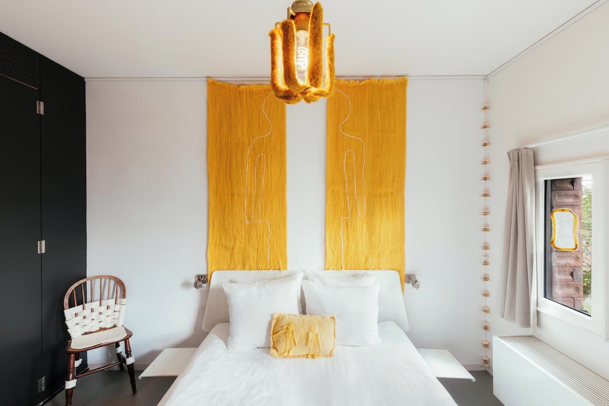 Un dormitorio con una cama, una silla, un ventanal y una pared con un diseño único.