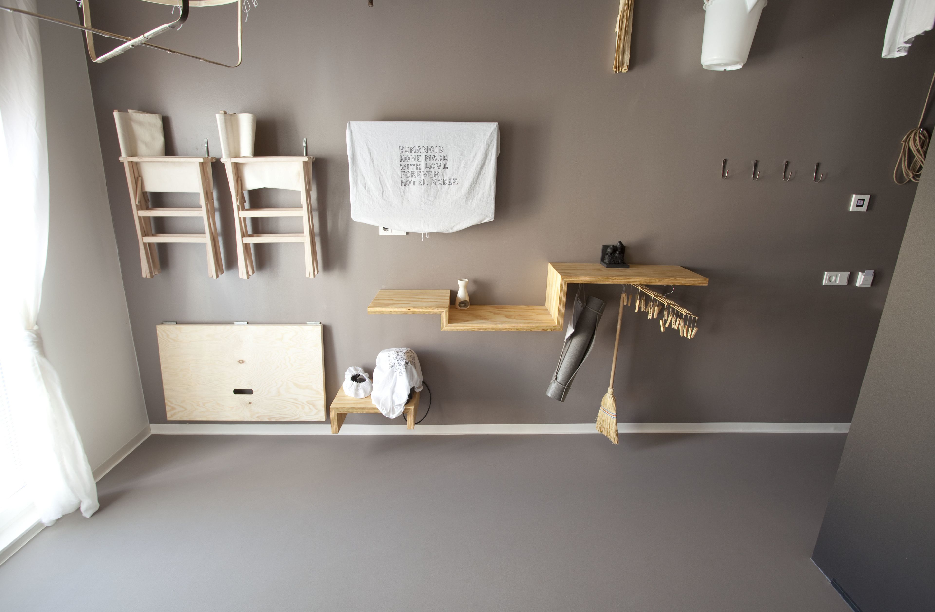 A room with a grey wall, wooden furniture, a white towel with text, and a broom.