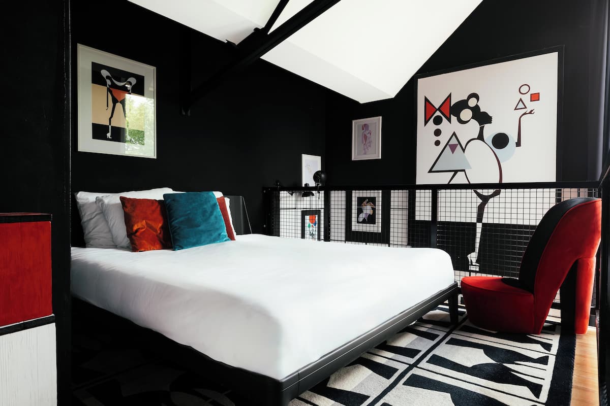 Un dormitorio moderno con una cama grande, una silla roja y arte abstracto en la pared.