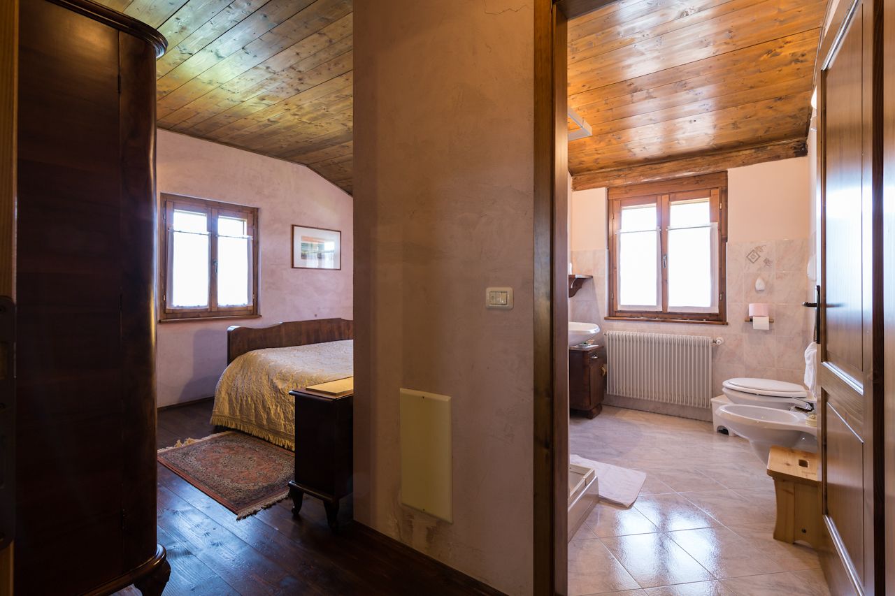 Ein Schlafzimmer mit einem Bett, einem Holzschrank und einem Fenster. Der Raum verfügt über eine Holzbalkendecke und eine Heizung.