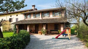 A two-story house with a gravel driveway, a wooden bench, and a red slide. - Agriturismo Borg da Ocjs (Cormons)