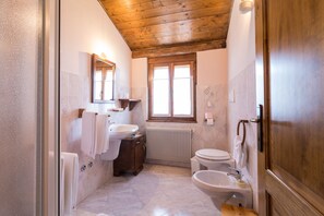 A bathroom with a wooden ceiling, a window, a radiator, a sink, a toilet, and a bathtub.