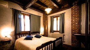A cozy bedroom with a wooden bed, two windows with curtains, a brick wall, and a radiator. - Agriturismo Borg da Ocjs (Cormons)